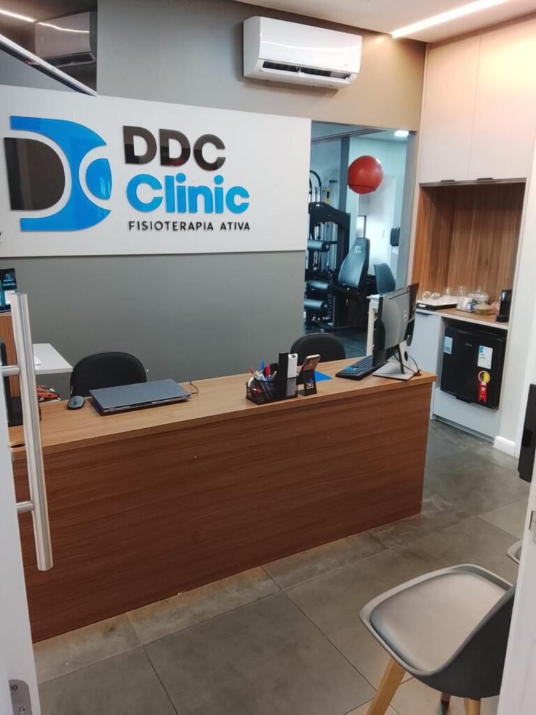 Entrada da recepção da DDC Clinic unidade São Caetano do Sul, mostrando balcão de madeira, logotipo na parede e vista para a sala de atendimento ao fundo.